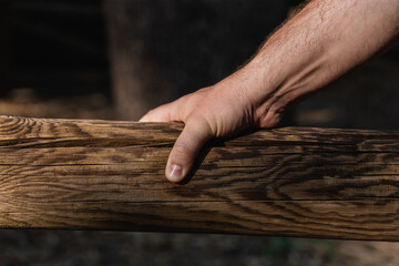 Hand of a middle-aged man holding a wooden log outdoors with natural light. Horizontal photography