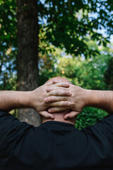 View from behind of mature man with little hair or alopecia with his hands on the nape of his neck.  Outdoor vertical photography outdoors with natural light. Concept of reflection and observation 