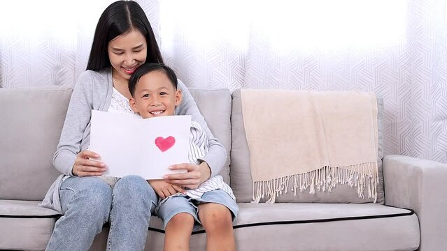 Lovely single mom getting present from kid happy mom enjoy reading handmade love card from small son cheerful embrace little child on mother day, valentine or birthday Love and care in family