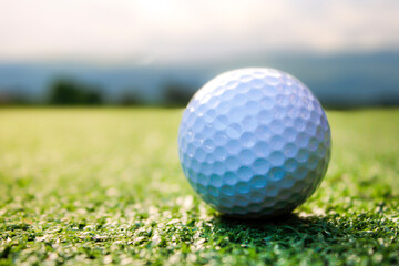 A golf ball is placed on the grass with a mountain view behind.