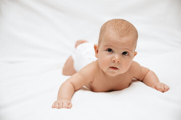 Little newborn baby in a diaper is trying to crawl on a white blanket.