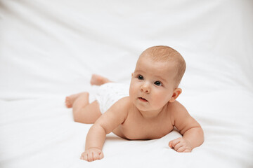 A newborn baby in a diaper is lying on stomach on a white background and looking to the side.
