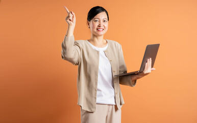 Portrait of  middle age Asian woman using laptop on brown background.
