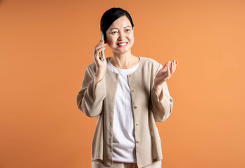 Portrait of middle age Asian woman using phone on brown background