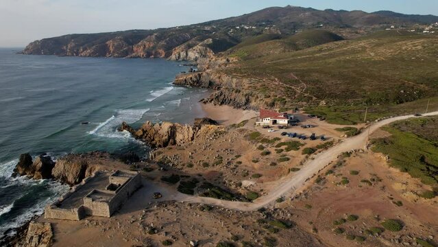 Aerial drone view of an yellow tuk-tuk rickshaw driving away from Fort of Guincho near Abano Beach in Guincho, Cascais, Portugal