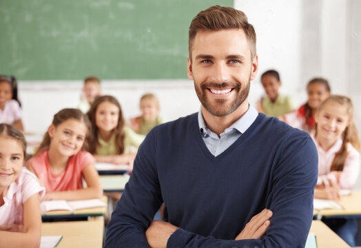 A male teacher in a jumper stands against the background of an elementary school classroom