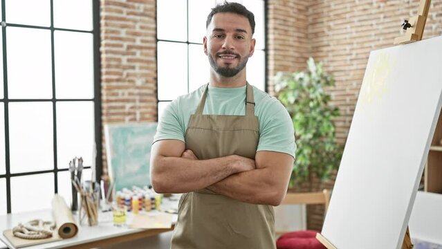 Young arab man artist standing with arms crossed gesture smiling at art studio