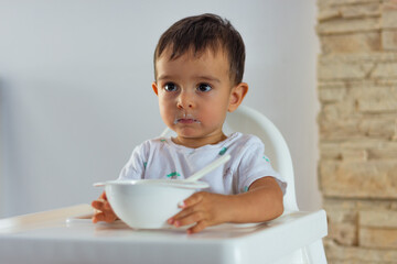 Toddler holding his plate while his face is smeared with yogurt