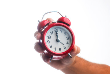 A man's hand holds a red round alarm clock. Retro alarm clock on a white background shows 12 o'clock.