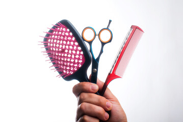 Hairdressing tools on a white background. The hairdresser holds scissors and a comb in his hand.