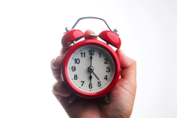 A beautiful red alarm clock in hand shows 6 o'clock in the morning.
Round alarm clock close-up on a white background.