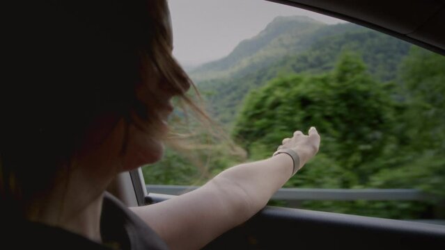 Pretty girl is driving a car, waving her hand in the wind. Open car window. A woman's road trip to nature in the mountains. Road Trip, freedom and holidays. A female enjoys the travel and vacation