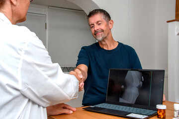 Naklejka na ściany i meble Patient and Doctor shake hands at an appointment. Xray of a patient' knee on a laptop whilst in talks with the consultant in the practise. 