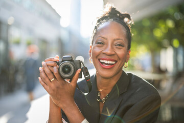 Portrait of smiling woman holding camera in the city
