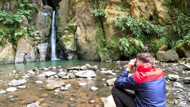 Photographer taking pictures of a waterfall called 'Cascada Salto del Cabrito' surrounded of rock, in Azores, Portugal