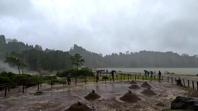 Geysers where the stew (Cozinhou) is cooked in the ground in the hot water inside the geysers in a hole, and lots of fumes, while lots of tourist see the scene, in Furnas, Azores, Portugal