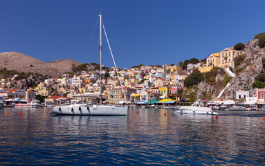 Fototapeta na wymiar White yacht against the backdrop of high mountains in the bay of Symi island.