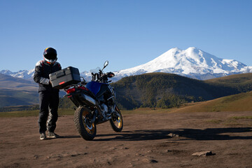 A motorcyclist with a motorcycle in the mountains against the background of snowy Elbrus. Copy...
