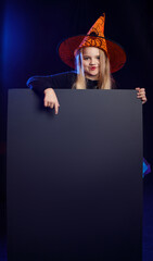 Little girl dressed as a witch with pumpkin on a dark background in the light of multi-colored spotlights