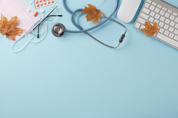 Modernize your medical experience online. Top view shot of keyboard, computer mouse, eyeglasses, stethoscope, clipboard, autumn leaves, medical mask on light blue background with promo space