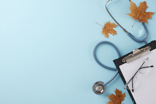 Scheduling a medical appointment for the fall. Top view photo of stethoscope, eyewear, dry fallen leaves, clipboard on light blue background with promo zone