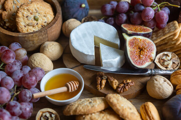 Figs, cheese, fruits, nuts, honey, cookies on a wooden tray.