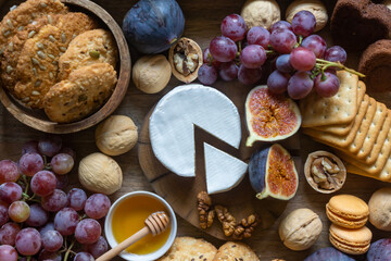 Figs, cheese, fruits, nuts, honey, cookies on a wooden tray.