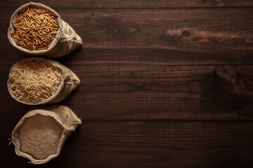 A trio of different stages of organic Rice (Oryza sativa) in a jute bag. Rice Bran, Rice, and Rice Flour on a dark wooden background. Top view.