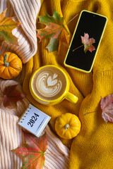 A cup of coffee and a phone on the table among pumpkins and autumn leaves. Calendar for 2024.