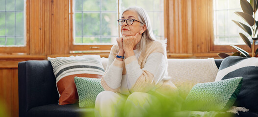 Thinking, reflection and senior woman on sofa in the living room with memory or dreaming face....