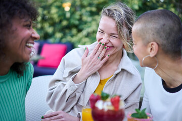 Three cheerful mature multiracial women laughing celebrating meeting outdoor. Group happy adult female best friends having fun drinking cocktail on terrace. Friendship relationships, alcohol drinks. - obrazy, fototapety, plakaty
