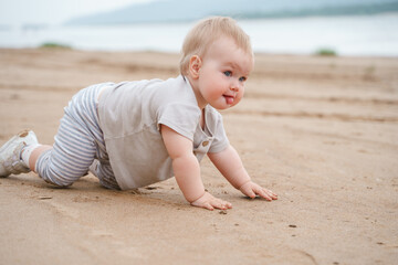 A one-year-old toddler sits on the beach of the sea in the evening after sunset