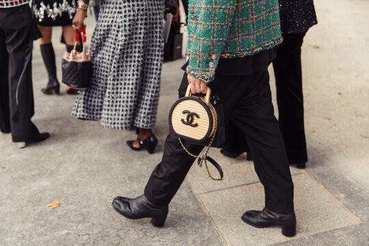 Woman walking on the street holding a beige bag, wearing black pants and green jacket  - Chanel Paris Fashion Week Street Style