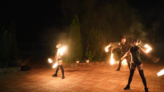 Fire performance show. Artists spin burning poles at night. Outdoor tribal dance with flames. Man and women dancers troupe act with torches at venue for tourists. Fire arts team juggling on festival.