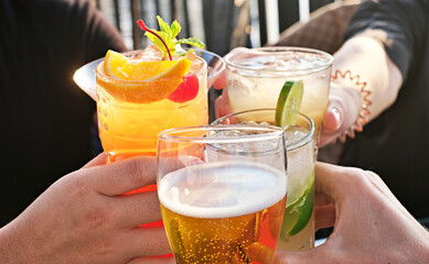 Friends toasting, saying cheers holding tropical blended fruit margaritas. Watermelon, beer and...