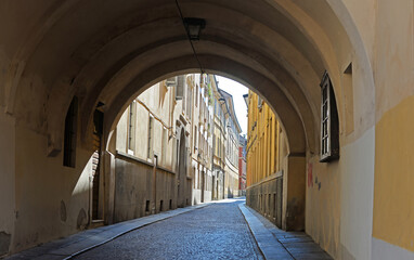 Empty, narrow street with typical old colorful houses and arch in the city centre of Parma, Italy