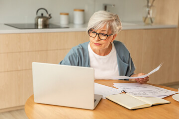 Middle aged senior woman sit with laptop and paper document, Pensive older mature lady reading...