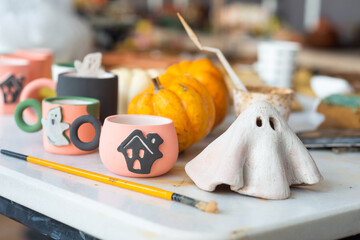Table cluttered with various unfinished Halloween crafts at a ceramics, pottery studio with tools,...