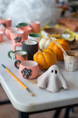 Table cluttered with various unfinished Halloween crafts at a ceramics, pottery studio with tools,...