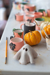 Table cluttered with various unfinished Halloween crafts at a ceramics, pottery studio with tools,...
