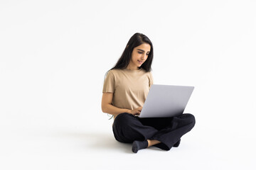 Naklejka premium Smiling beautiful young indian woman wearing casual outfit using laptop on white wall background
