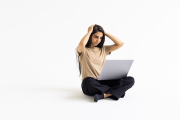 Disturbed stressed young indian woman working on laptop standing over white background.