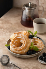 Homemade choux pastry rings with cottage cheese cream and blackberry decorated mint leaves on beige kitchen background with tea