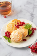 Cottage cheese pancakes, syrniki, ricotta fritters with fresh berries and sour cream and tea on white marble background close up. Healthy and delicious breakfast, high key