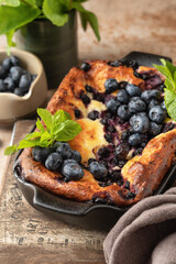 Cottage cheese casserole with blueberries and mint leaves decoration in baking dish close up on brown textured background