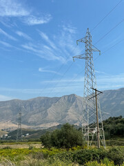Obraz premium Overhead line pylons, high voltage pylons in meadow with mountains on background