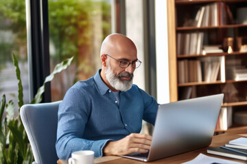 A middle-aged man uses a laptop at home, delving into research on financial literacy, showcasing his dedication to personal finance.