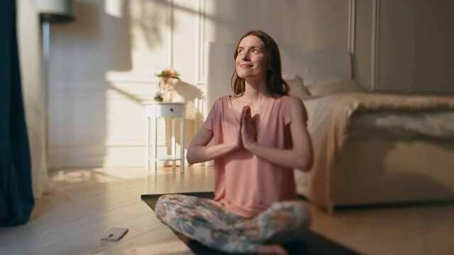 Smiling girl sitting lotus asana in morning sunlight. Carefree woman meditating