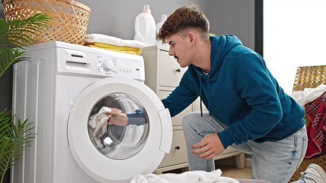 Young hispanic man washing clothes holding dirty t shirt at laundry room