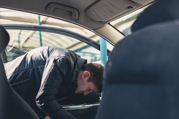 A young man vacuums the interior of a car. - obrazy, fototapety, plakaty